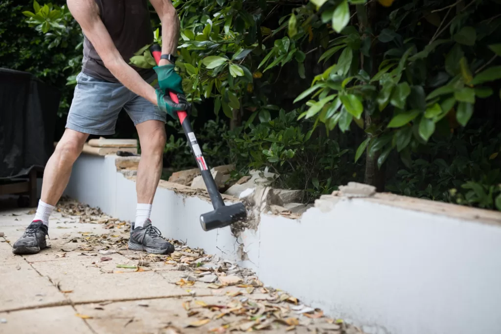 asian man holding a big hammer demolishing a side walk wall