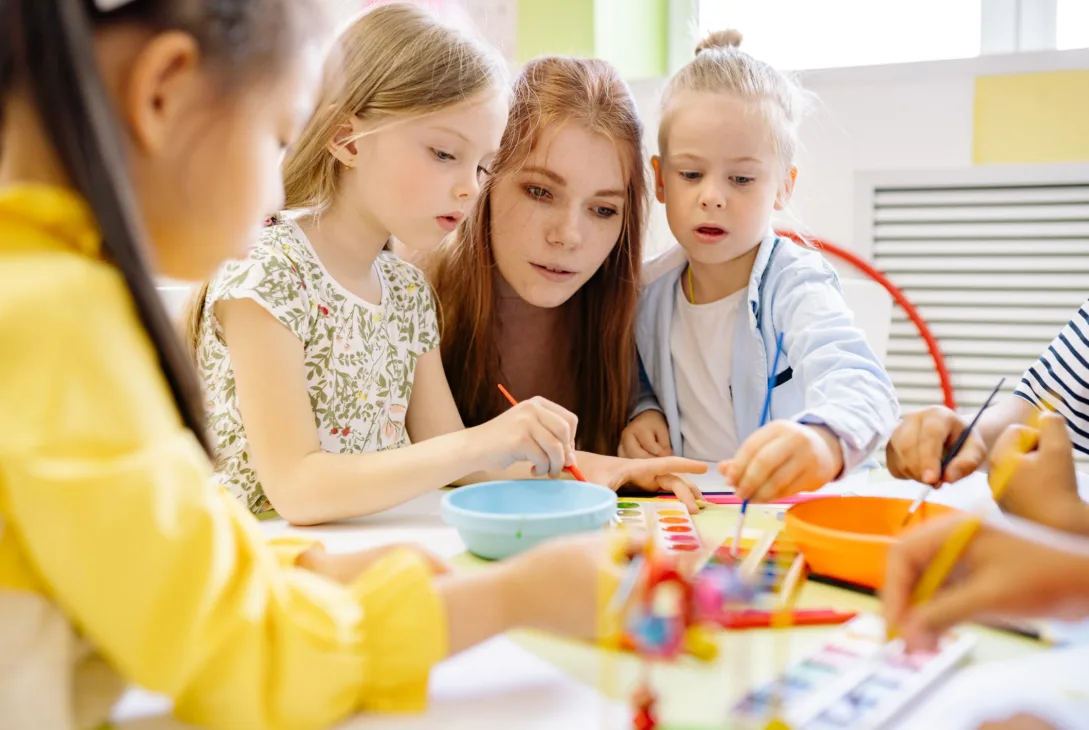 teacher assisting a young student in a classroom at an early years center, engaging in activities aligned with the international primary curriculum