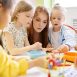 teacher assisting a young student in a classroom at an early years center, engaging in activities aligned with the international primary curriculum