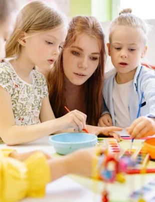 teacher assisting a young student in a classroom at an early years center, engaging in activities aligned with the international primary curriculum