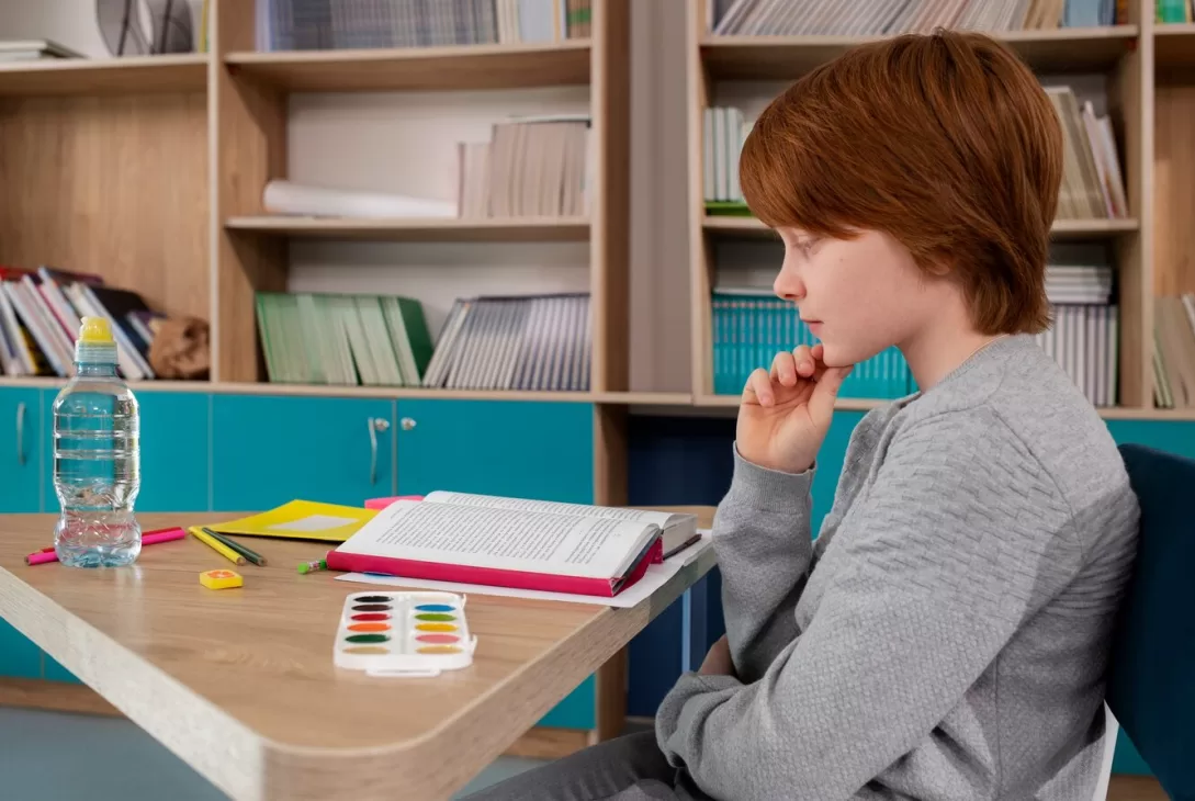 ginger-haired boy studying at his desk pondering at his homework