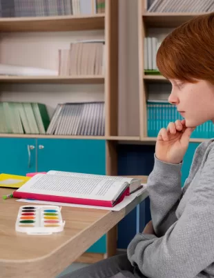 ginger-haired boy studying at his desk pondering at his homework