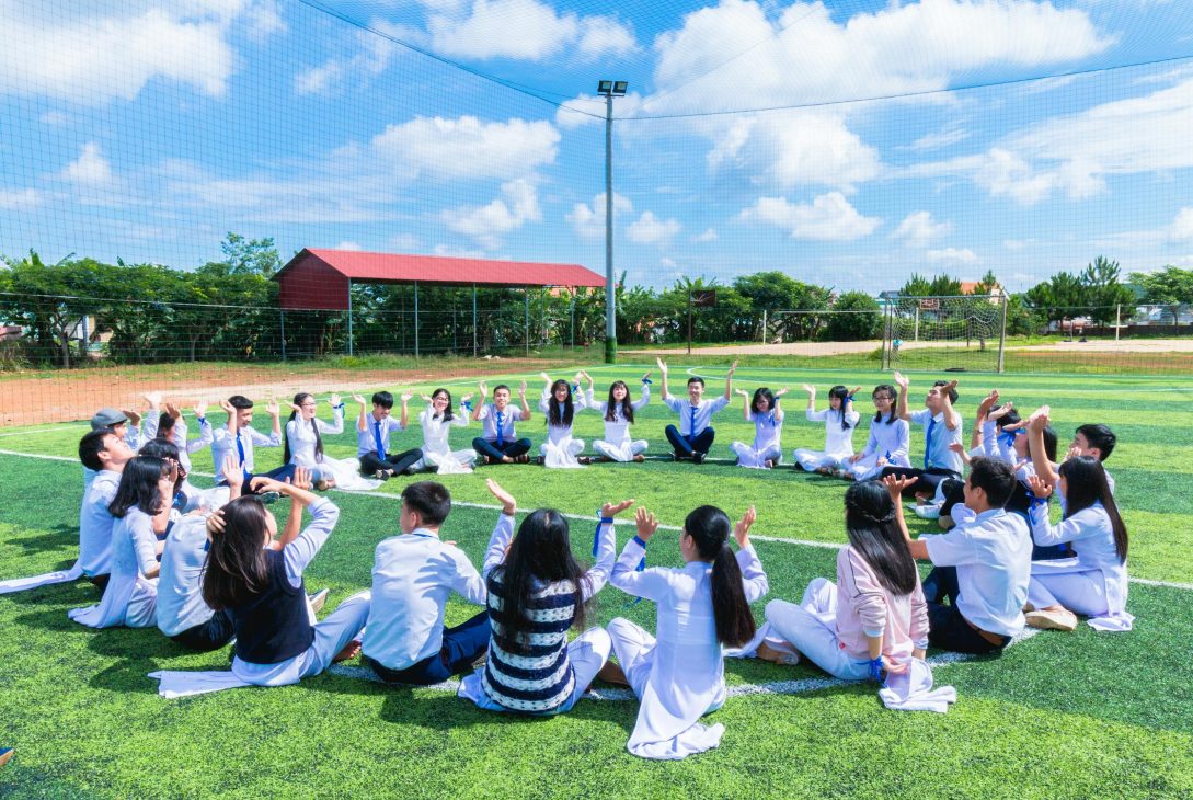 a group of international primary school students in Malaysia lifting hands up at a field