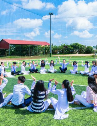 a group of international primary school students in Malaysia lifting hands up at a field