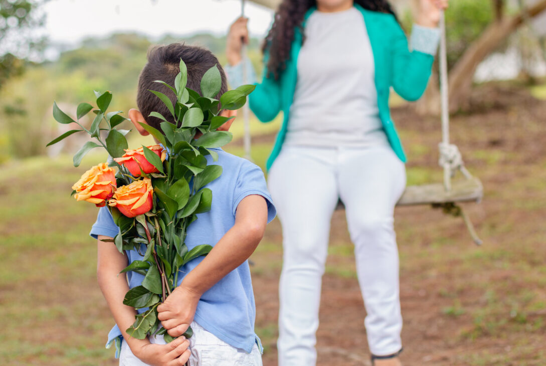A boy discreetly hiding a beautiful flower bouquet to surprise his mom for Mother's Day.