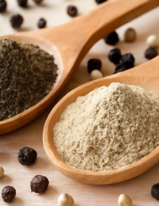 Black pepper powder and white pepper powder in wooden spoons on a rustic surface