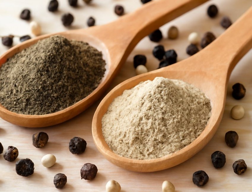 Black pepper powder and white pepper powder in wooden spoons on a rustic surface