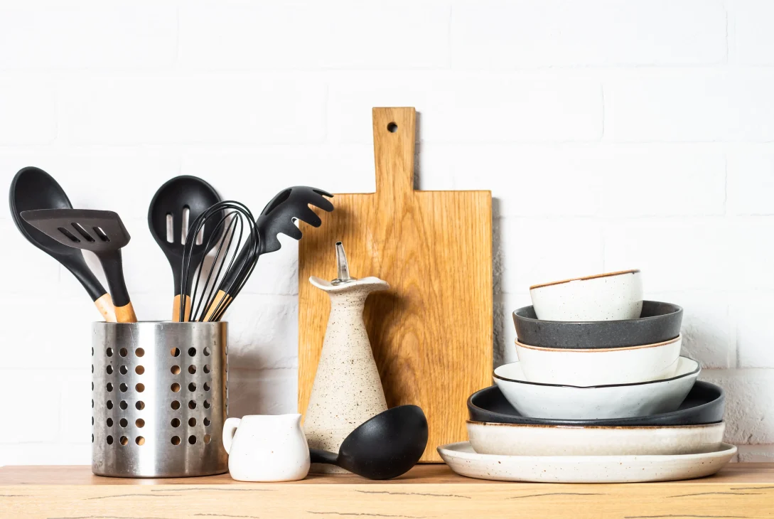 Stylish dinner plates, cutlery set, and kitchen utensils on a wooden counter at white background.