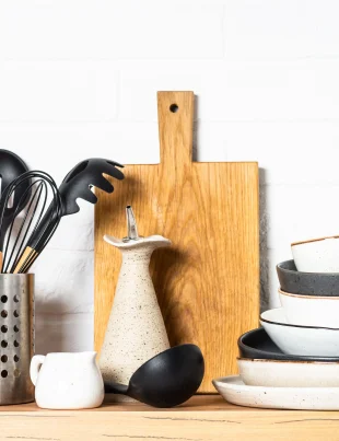 Stylish dinner plates, cutlery set, and kitchen utensils on a wooden counter at white background.