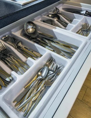 Organized kitchen drawer with stainless steel spoons, forks, and knives in a white cutlery tray.