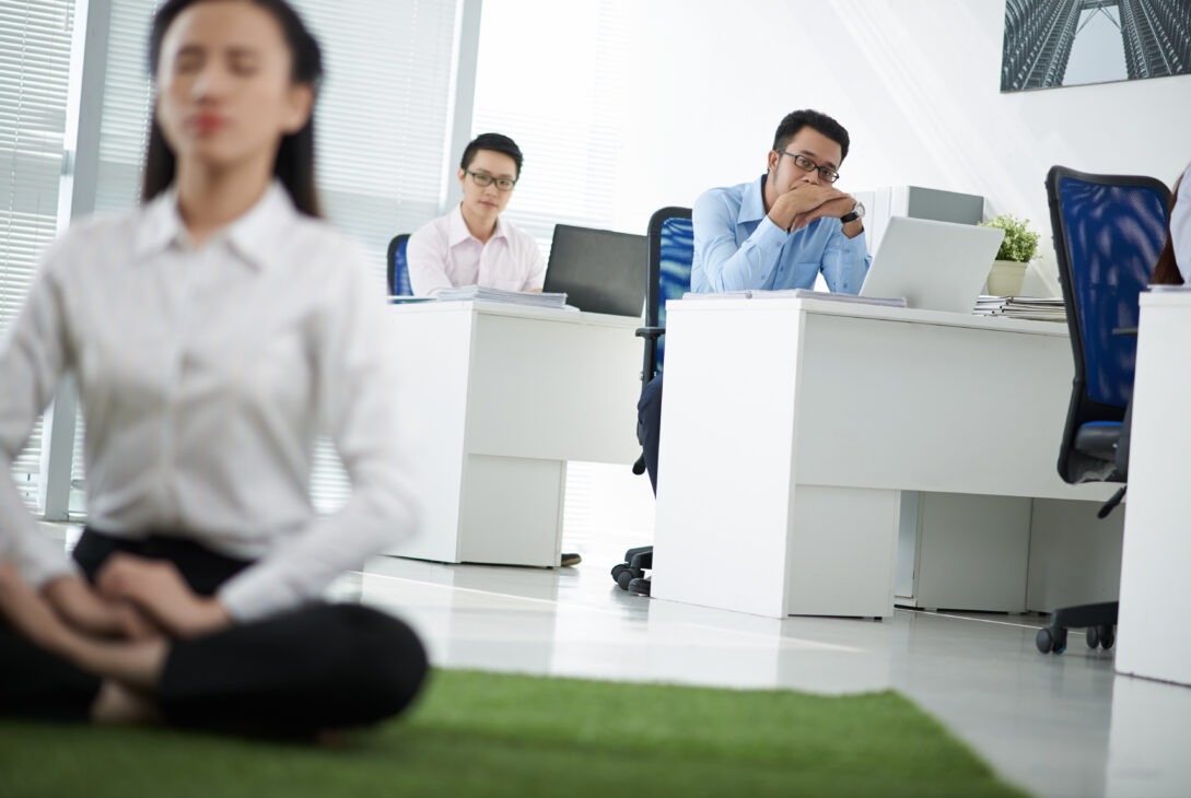 Employee meditating in an office setting while coworkers observe, representing a mental wellness program in a Singapore workplace