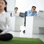 Employee meditating in an office setting while coworkers observe, representing a mental wellness program in a Singapore workplace