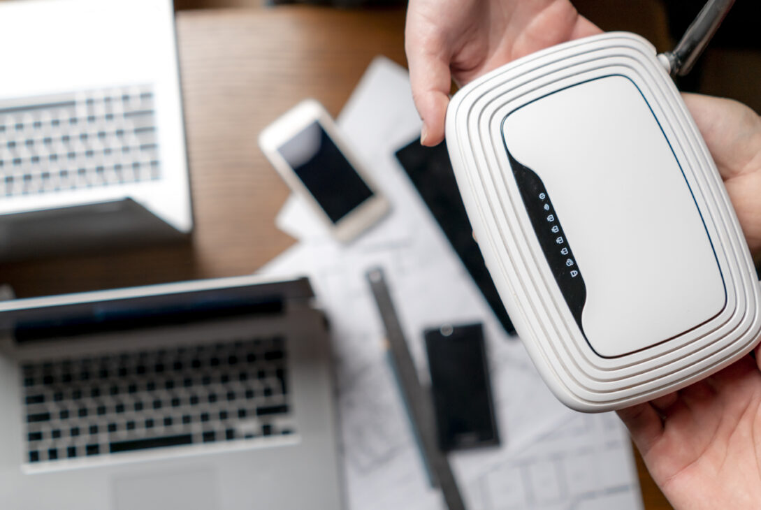 Person holding a WiFi router surrounded by laptops and smartphones on a desk