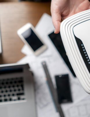 Person holding a WiFi router surrounded by laptops and smartphones on a desk