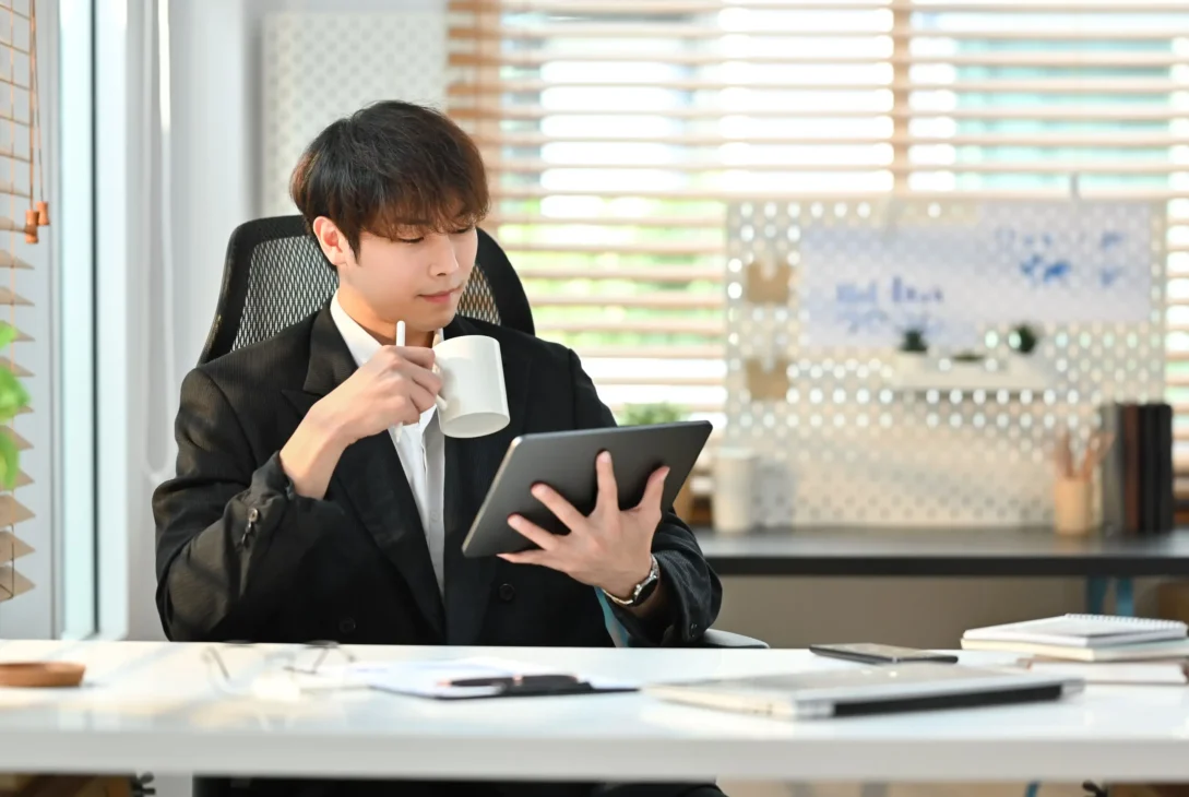 Young businessman working from home on a tablet, drinking coffee, embodying flexibility and financial freedom.
