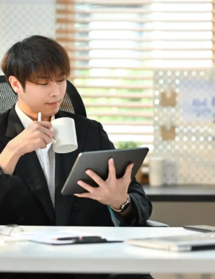 Young businessman working from home on a tablet, drinking coffee, embodying flexibility and financial freedom.